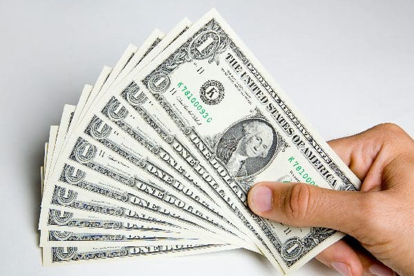 A hand holding a fanned-out stack of one-dollar bills.